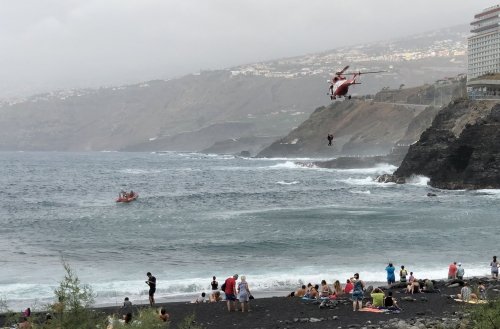 Rescue helicopter lifting persons out of the ocean, notice the volcanic black beach