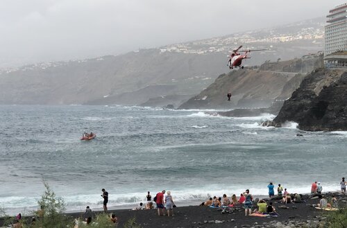Rescue helicopter lifting persons out of the ocean, notice the volcanic black beach