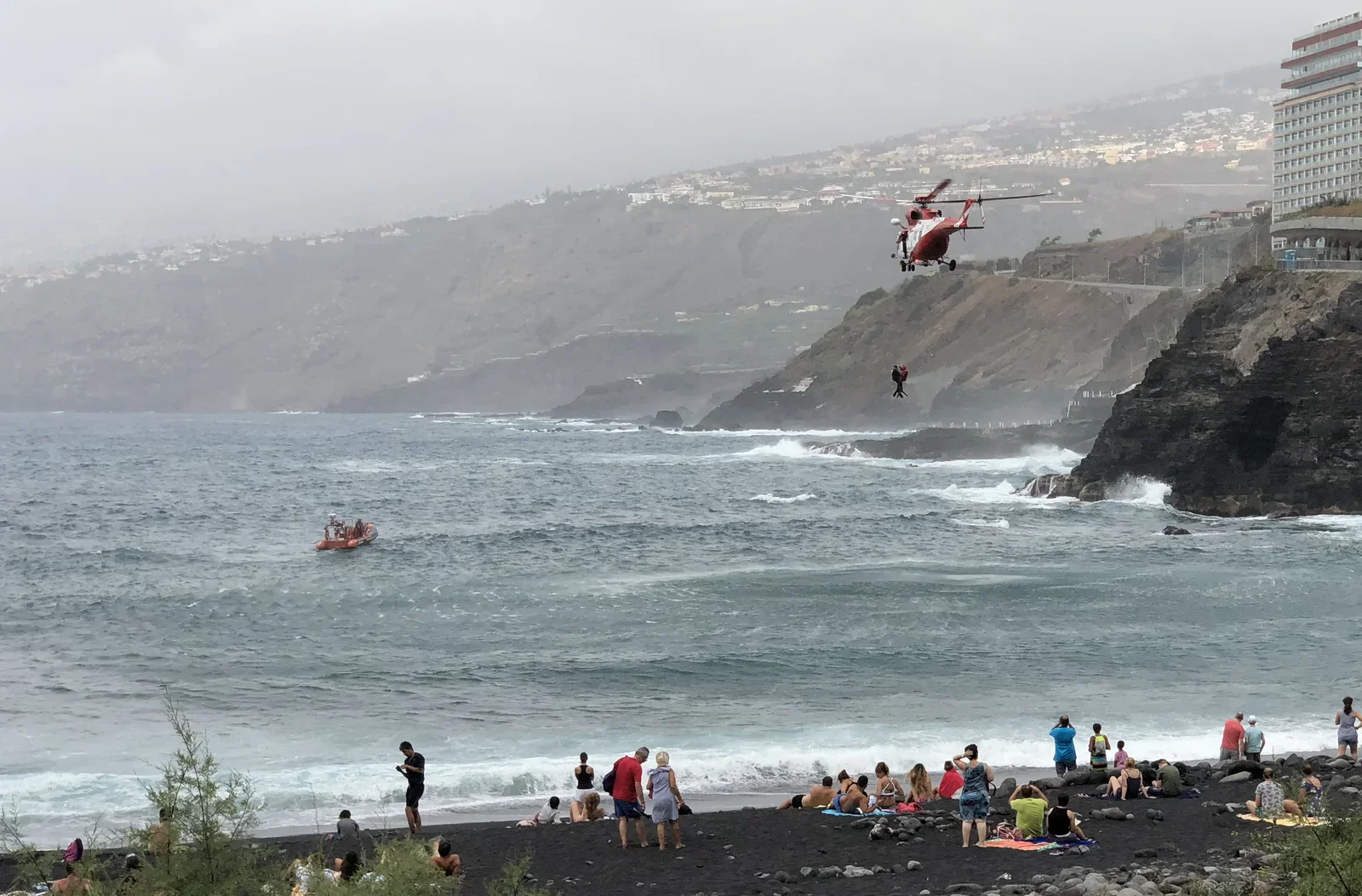 Rescue helicopter lifting persons out of the ocean, notice the volcanic black beach