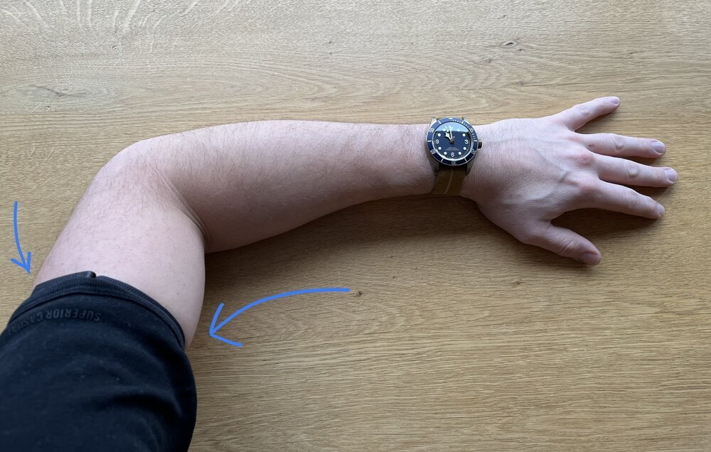 Gedragen op de biceps, verbergt WHOOP zich gemakkelijk onder je kleding - aangegeven met blauwe pijlen - waardoor je polsen vrij blijven voor mechanische horloges